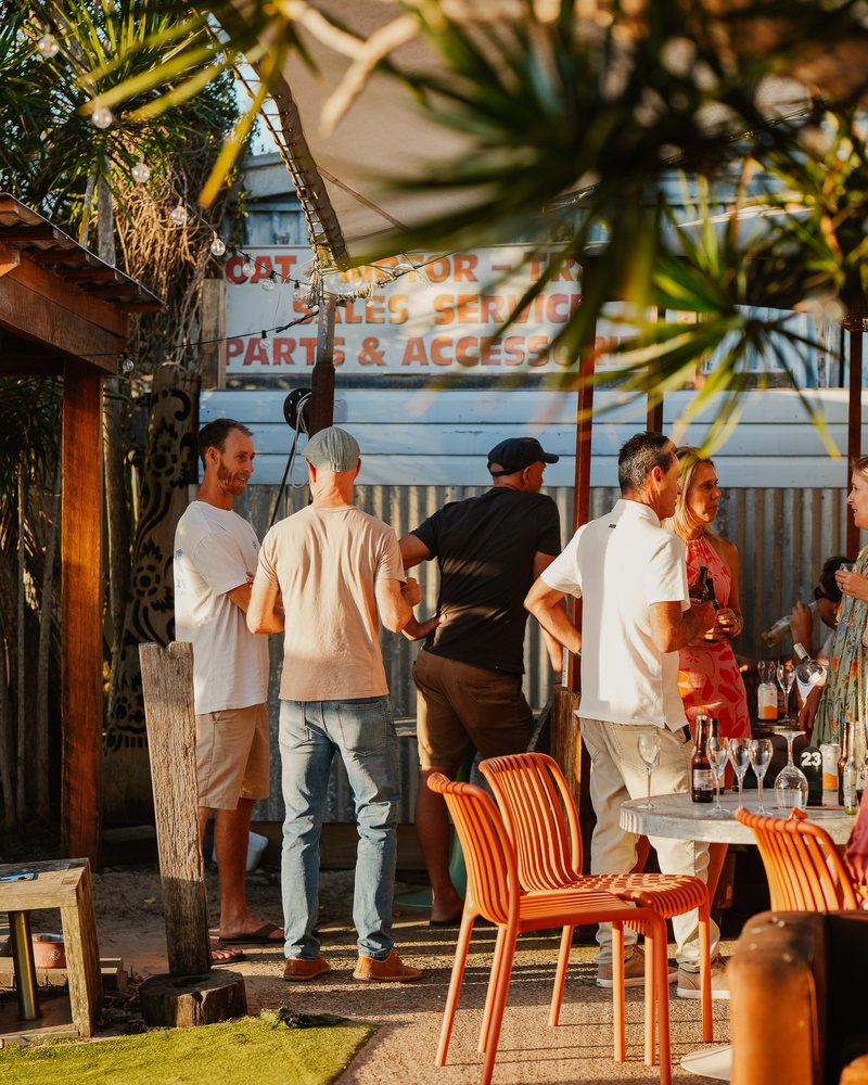 A group gathered in the garden at golden hour with drinks and orange chairs